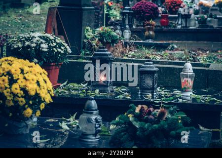 tombe decorate con lanterne, candele accese, fiori colorati di crisantemo, simboli cattolici Foto Stock