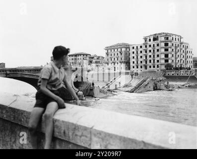 1945 , 26 aprile , VERONA , VENETO , ITALIA : DALLA DIDASCALIA ORIGINALE: »Quinta Armata americana a Verona . Il ragazzo italiano si affaccia sul fiume Adige e sul ponte della Vittoria che i tedeschi nazisti e fascisti italiani hanno fatto esplodere durante la fuga". La notte del 25 aprile 1945, quando fu estratta e fatta esplodere dai soldati tedeschi in ritirata, un'esplosione che lasciò intatta solo l'arco verso la città. In questa foto scattata da Lungadige Panvinio si può anche vedere la devastazione di tutte le case di fronte al ponte che si affaccia su Lungadige Giamomo Matteotti ( come oggi rinominato ) e Lungadige Camp Foto Stock