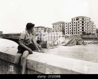 1945 , 26 aprile , VERONA , VENETO , ITALIA : DALLA DIDASCALIA ORIGINALE: »Quinta Armata americana a Verona . Il ragazzo italiano si affaccia sul fiume Adige e sul ponte della Vittoria che i tedeschi nazisti e fascisti italiani hanno fatto esplodere durante la fuga". La notte del 25 aprile 1945, quando fu estratta e fatta esplodere dai soldati tedeschi in ritirata, un'esplosione che lasciò intatta solo l'arco verso la città. In questa foto scattata da Lungadige Panvinio si può anche vedere la devastazione di tutte le case di fronte al ponte che si affaccia su Lungadige Giamomo Matteotti ( come oggi rinominato ) e Lungadige Camp Foto Stock