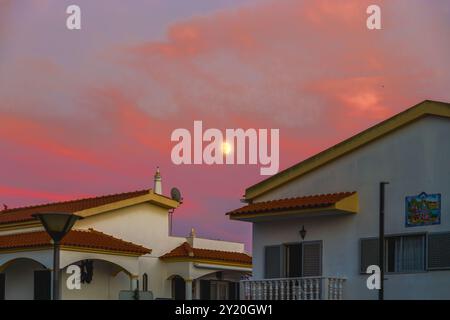 Il chiaro di luna risplende attraverso nuvole colorate serali sopra le case di periferia. Foto Stock