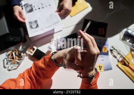 Mano che tiene la sigaretta con la punta bruciata sul tavolo disseminata di prove. Documenti, marcatori numerati e strumenti scientifici visibili, che indicano l'indagine in corso Foto Stock