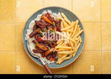 Saltado di Lomo con patatine fritte e riso su sfondo piastrelle gialle, piatto tradizionale peruviano Foto Stock