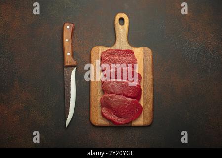 Bistecche di manzo crude stese su un tagliere di legno con vista dall'alto del coltello Foto Stock