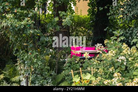 Comoda panca in un parco con coperta rosa, circondata da lussureggianti alberi e vegetazione, creando un rilassante luogo all'aperto, concetto di serenità all'aperto Foto Stock
