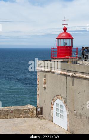 Faro rosso su una piattaforma costiera con mare sullo sfondo e persone che si godono la vista, Fort Sao Miguel Acanjo, Farol de Nazare, Faro di Foto Stock