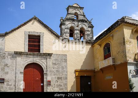 Vecchia chiesa con porta d'ingresso in legno incorniciata da facciata in pietra e campanile in una giornata di sole nella città vecchia, Cartagena, Colombia, Sud America Foto Stock