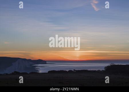 L'alba di dicembre da Seaford Head, guardando verso sud-est sul canale della Manica con il faro Belle Tout visibile in lontananza sulla cima della scogliera Foto Stock