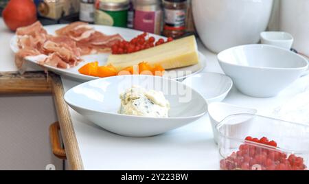 Assortimento di ingredienti per pasti gourmet, con formaggi, affettati, frutta e verdura varie, allestito su un bancone della cucina, preparazioni culinarie Foto Stock