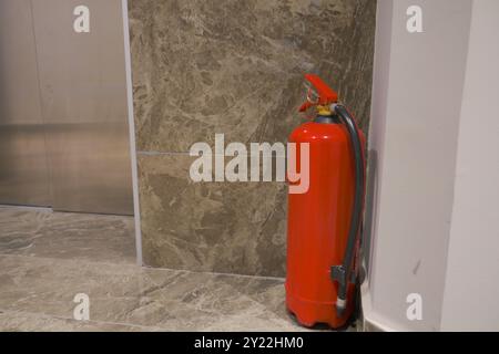 Un estintore rosso situato in un ambiente interno moderno per la sicurezza e l'uso di emergenza Foto Stock