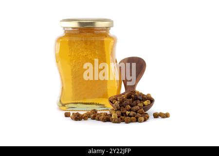 Primo piano di un vaso di vetro riempito con miele dorato e un cucchiaio di legno con pane alle api, che presenta prodotti biologici per l'apicoltura su sfondo bianco Foto Stock