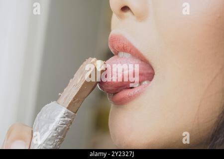 Primo piano ritratto di una donna asiatica che mangia una barretta di cioccolato con involucro di lamina mentre sorride mentre si gode il suo spuntino. Foto Stock