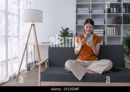 la donna si rilassa a casa, sdraiandosi sul divano con il suo smartphone, godendosi un momento tranquillo di svago e connessione nel suo confortevole spazio abitativo Foto Stock