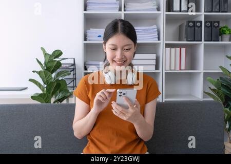 la donna si rilassa a casa, sdraiandosi sul divano con il suo smartphone, godendosi un momento tranquillo di svago e connessione nel suo confortevole spazio abitativo Foto Stock