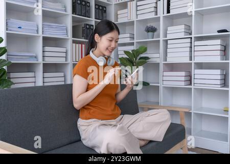 la donna si rilassa a casa, sdraiandosi sul divano con il suo smartphone, godendosi un momento tranquillo di svago e connessione nel suo confortevole spazio abitativo Foto Stock