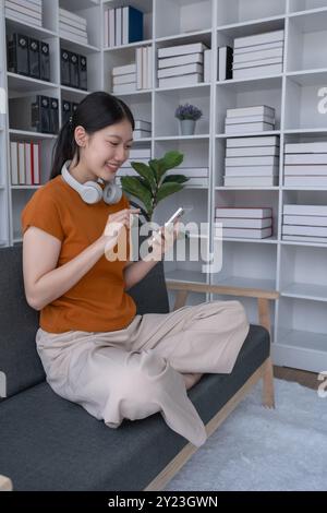 la donna si rilassa a casa, sdraiandosi sul divano con il suo smartphone, godendosi un momento tranquillo di svago e connessione nel suo confortevole spazio abitativo Foto Stock