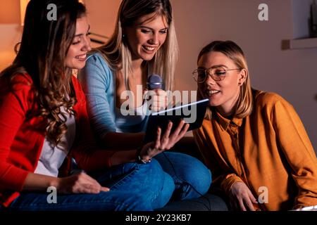 Tre amiche che si divertono a giocare a karaoke a casa. Foto Stock