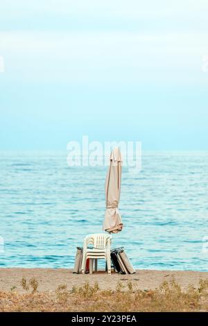 Ombrellone ripiegato, sedia e altri accessori da spiaggia in riva al mare, attenzione selettiva Foto Stock