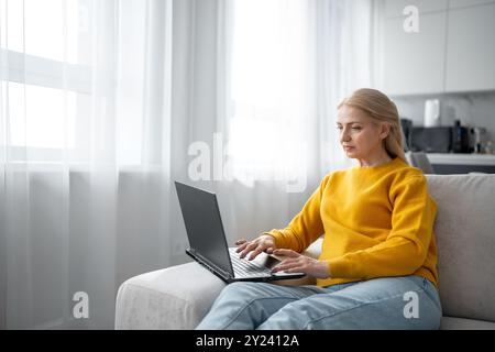 Una donna bionda lavora con molta attenzione dal suo ufficio domestico, scrivendo su un notebook Foto Stock