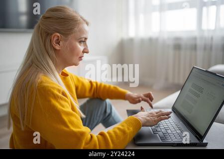Una donna bionda lavora con molta attenzione dal suo ufficio domestico, scrivendo su un notebook Foto Stock
