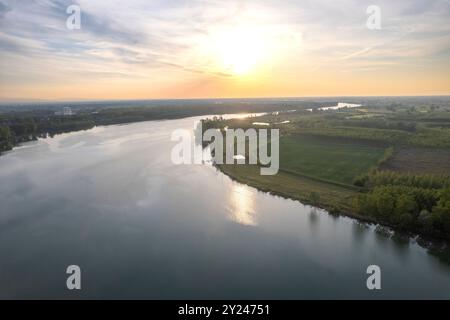 Il tranquillo sentiero di ghiaia si snoda lungo la tranquilla riva di un lago al tramonto, con una luce dorata che si riflette nelle acque calme, creando una scena tranquilla, po R. Foto Stock