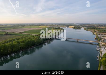 Il tranquillo sentiero di ghiaia si snoda lungo la tranquilla riva di un lago al tramonto, con una luce dorata che si riflette nelle acque calme, creando una scena tranquilla, po R. Foto Stock