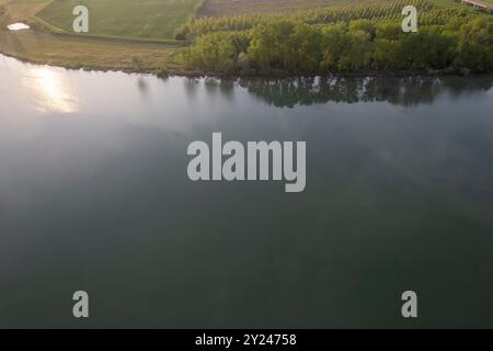 Il tranquillo sentiero di ghiaia si snoda lungo la tranquilla riva di un lago al tramonto, con una luce dorata che si riflette nelle acque calme, creando una scena tranquilla, po R. Foto Stock