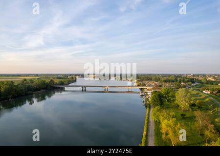 Il tranquillo sentiero di ghiaia si snoda lungo la tranquilla riva di un lago al tramonto, con una luce dorata che si riflette nelle acque calme, creando una scena tranquilla, po R. Foto Stock