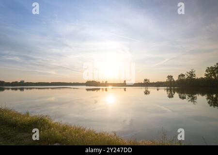 Il tranquillo sentiero di ghiaia si snoda lungo la tranquilla riva di un lago al tramonto, con una luce dorata che si riflette nelle acque calme, creando una scena tranquilla, po R. Foto Stock