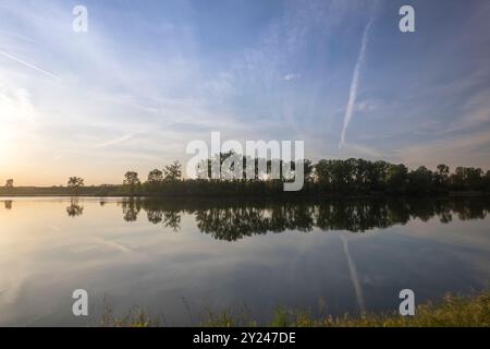 Il tranquillo sentiero di ghiaia si snoda lungo la tranquilla riva di un lago al tramonto, con una luce dorata che si riflette nelle acque calme, creando una scena tranquilla, po R. Foto Stock