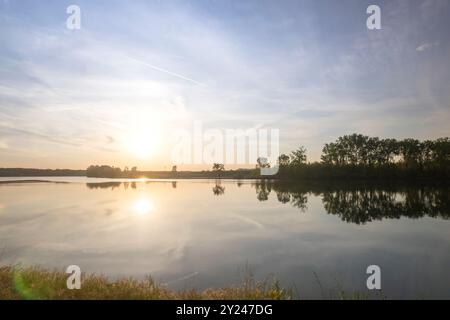 Il tranquillo sentiero di ghiaia si snoda lungo la tranquilla riva di un lago al tramonto, con una luce dorata che si riflette nelle acque calme, creando una scena tranquilla, po R. Foto Stock