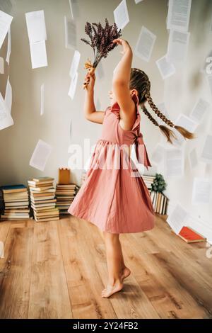 Ragazza in un abito rosa che si intreccia di fiori, circondata da pagine volanti Foto Stock