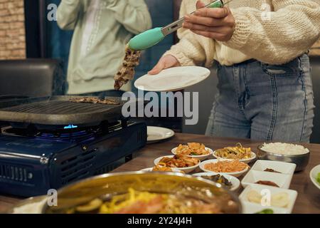 La donna asiatica cucina la carne nella padella sulla stufa nelle regate Foto Stock