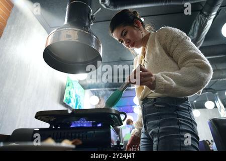 La donna asiatica cucina la carne nella padella sulla stufa nelle regate Foto Stock