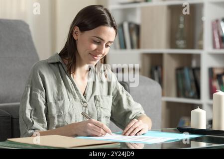 Donna felice che legge e firma documenti cartacei a casa Foto Stock