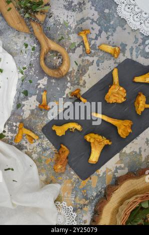 Tavolo con vista dall'alto - funghi canterelle dorati su un tagliere nero, erbe verdi, tovaglioli bianchi e tovaglie. Foto Stock