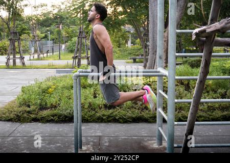 Vista laterale di un giovane che fa la calistenica in un parco nel centro di Bangkok, Thailandia Foto Stock