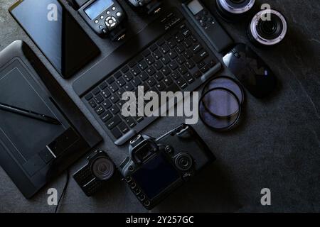 Workstation fotografica digitale su sfondo nero. Vista dall'alto di fotocamera digitale, flash, obiettivo e computer portatile. Foto Stock