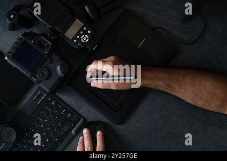 Workstation fotografica digitale su sfondo nero. Vista dall'alto di fotocamera digitale, flash, obiettivo e computer portatile. Foto Stock