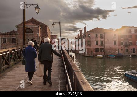 Venezia, Italia - 18 aprile 2024: Una coppia di anziani cammina al tramonto sul ponte di Venezia Foto Stock