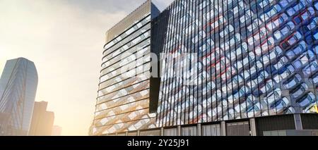 Moderna sede centrale del produttore di auto elettriche e ibride. Edificio per uffici in vetro che riflette file di veicoli nuovi. Architettura aziendale per sostenere Foto Stock