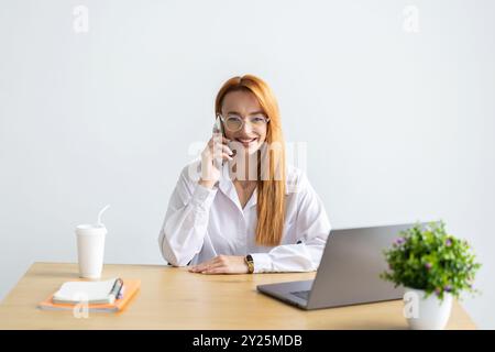 Donna felice che usa il telefono cellulare e i computer portatili per il lavoro. Donna d'affari sicura che lavora da casa. Ufficio domestico. Foto Stock