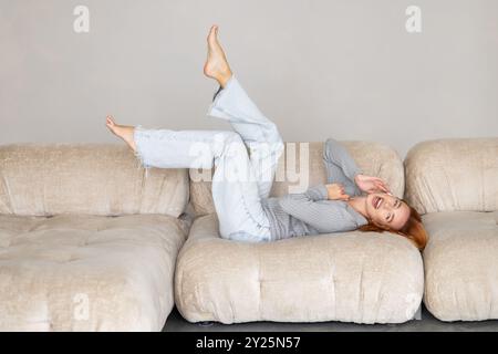 Una giovane e tranquilla donna sdraiata su un comodo divano morbido con gambe sollevate si sente spensierata. Trascorri un fine settimana tranquillo da sola a casa. Giorno libero, niente stress, felice proprietario fe Foto Stock