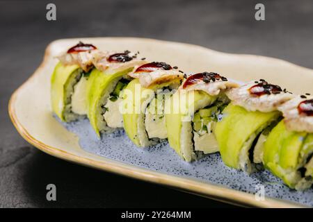 Sushi in anguilla con ripieno cremoso, condito con salsa salata e semi di sesamo su un piatto elegante Foto Stock