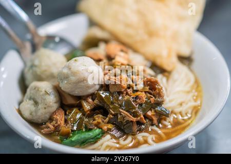 Una ciotola di spaghetti condita con polpette, carne grattugiata e verdure a foglia verde, serviti con cracker croccanti a lato. Foto Stock