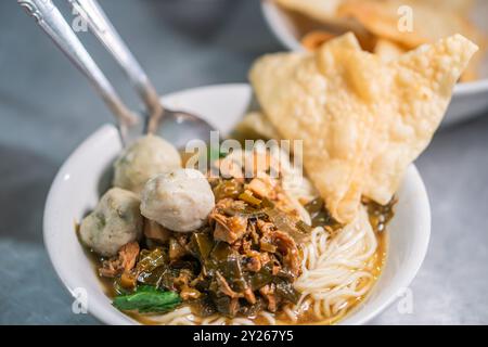 Una ciotola di spaghetti condita con polpette, carne grattugiata e verdure a foglia verde, serviti con cracker croccanti a lato. Foto Stock