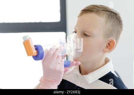 Ragazzo con asma allergica, inalando il farmaco attraverso Spacer mentre è seduto nell'ufficio medico. Foto Stock