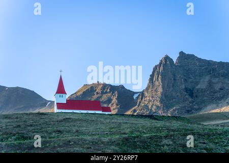 Una classica scena islandese: Una piccola chiesa dal tetto rosso si erge orgogliosamente su uno sfondo di aspre montagne. La vivace chiesa contrasta splendidamente Foto Stock