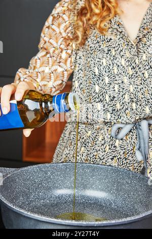 Una donna versa l'olio extra vergine d'oliva in una padella per preparare la cottura Foto Stock