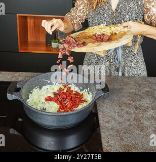 Pomodori secchi, olive e carciofi vengono aggiunti alla teglia con cipolle per un piatto ricco e saporito Foto Stock