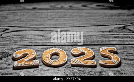 Primo piano di pani di zenzero dorati al forno per i saluti di buon anno 2025 su legno scuro. Dolci biscotti natalizi ornamentali su sfondo naturale bianco e nero. Foto Stock